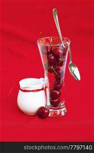 milk jug with a ribbon glass of cherry and spoon on a red background
