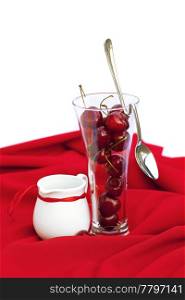 milk jug with a ribbon glass of cherry and spoon on a red background
