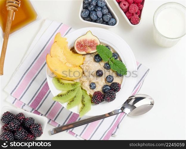 milk, plate with oatmeal porridge and fruit, honey in a bowl on a white table. Healthy breakfast