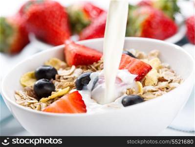 milk pouring into bowl of cereals with fresh berries