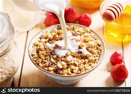 milk pouring into bowl of muesli on wooden table