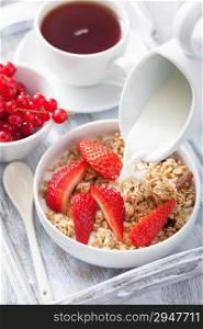 milk pouring over granola with strawberry for breakfast