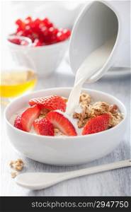 milk pouring over granola with strawberry for breakfast