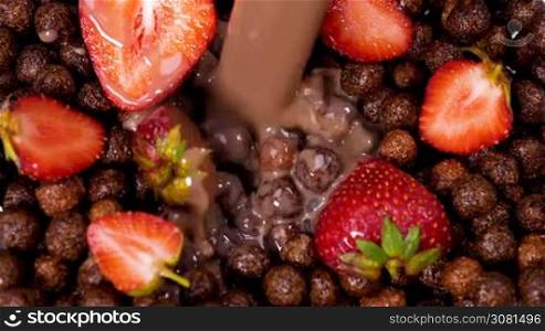 Milk with chocolate flowing on cocoa cereals with strawberries. Healthy eating for breakfast concept. Slow motion footage.