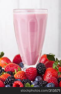 Milkshake glass with fresh summer berries smoothie on wooden background.Strwberries and raspberies with blueberries and blackberries.