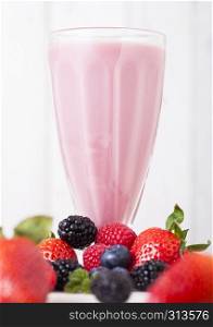 Milkshake glass with fresh summer berries smoothie on wooden background.Strwberries and raspberies with blueberries and blackberries.