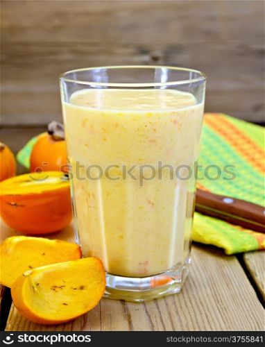 Milkshake in a glass with persimmons, napkin, knife on background wooden plank
