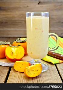 Milkshake in glass goblet with persimmons, napkin, knife on background wooden plank