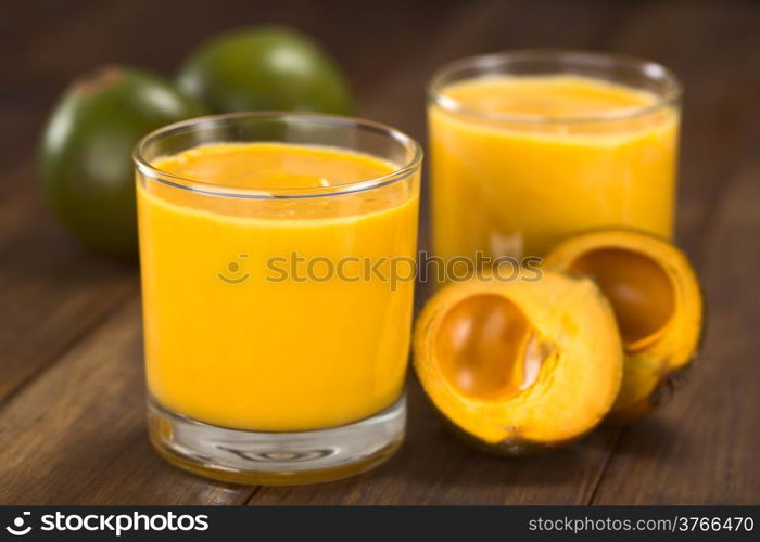 Milkshake made of the Peruvian fruit called lucuma (lat. Pouteria lucuma) served in glass with lucuma fruits around (Selective Focus, Focus on the front of the glass rim)