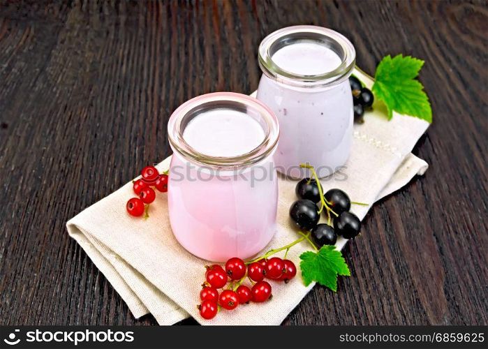 Milkshake with red and black currants in glass jars on a napkin with berries on a background of a dark wooden board