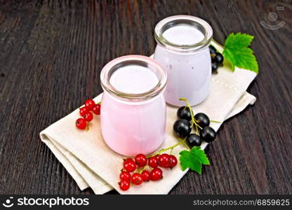 Milkshake with red and black currants in glass jars on a napkin with berries on a background of a dark wooden board