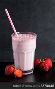 Milkshake with strawberries on a black background. Summer drink in a glass with a paper straw. Place for text.. Milkshake with strawberries on black background. Summer drink in a glass with a paper straw.