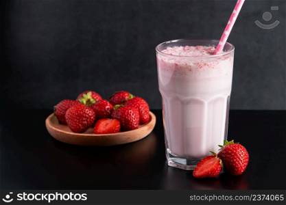 Milkshake with strawberries on a black background. Summer drink in a glass with a paper straw. Place for text.. Milkshake with strawberries on black background. Summer drink in a glass with a paper straw.