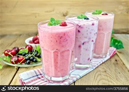 Milkshakes with black currant, cherry, raspberry in glass on the background of wooden boards