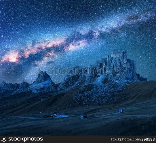 Milky Way above mountains at night in summer. Landscape with alpine mountain valley, road, sky with bright milky way and stars, buildings on the hill, rocks. Passo Giau in Dolomites, Italy. Space