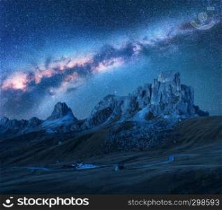 Milky Way above mountains at night in summer. Landscape with alpine mountain valley, road, sky with bright milky way and stars, buildings on the hill, rocks. Passo Giau in Dolomites, Italy. Space