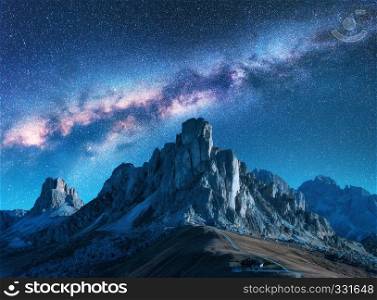 Milky Way above mountains at night in summer. Landscape with alpine mountain valley, blue sky with milky way and stars, buildings on the hill, rocks. Aerial view. Passo Giau in Dolomites, Italy. Space