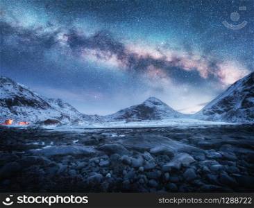 Milky Way above snow covered mountains and stone beach in winter at night in Lofoten Islands, Norway. Arctic landscape with blue starry sky, sea coast, snowy rocks, galaxy. Beautiful space and nature