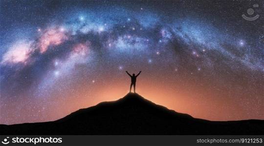 Milky Way and happy man on mountain peak at starry night. Silhouette of guy with raised up arm on the hill, sky with stars, yellow light in Nepal. Galaxy. Space landscape with milky way arch
