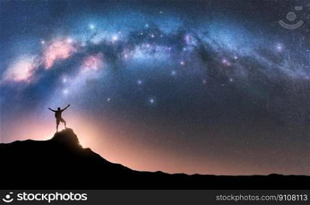 Milky Way and happy man with backpack on mountain peak at night. Silhouette of guy with raised up arm on the hill, sky with stars, yellow light in Nepal. Galaxy. Space landscape with milky way arch