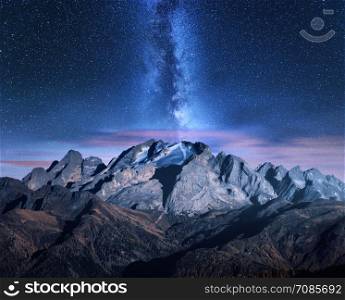 Milky Way and mountains at starry night in autumn. Amazing landscape with alpine snowy mountains, trees, sky with clouds, milky way and stars, high rocks. Dolomites, Italy. Space. Beautiful nature