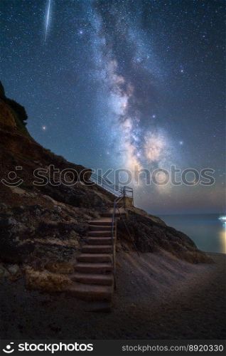 Milky Way and stairs on the beach at summer starry night. Summer in Lefkada, Greece. Beautiful landscape with sky with bright stars and milky way, meteorite, steps, sandy beach, rock, sea coast. Space. Milky Way and stairs on the beach at summer starry night