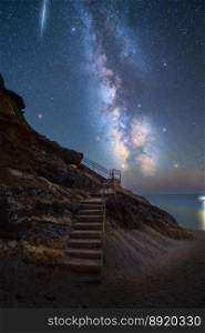 Milky Way and stairs on the beach at summer starry night. Summer in Lefkada, Greece. Beautiful landscape with sky with bright stars and milky way, meteorite, steps, sandy beach, rock, sea coast. Space. Milky Way and stairs on the beach at summer starry night