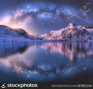 Milky Way arch above sea coast and snow covered mountains in winter at night. Lofoten Islands, Norway. Arctic landscape with blue starry sky, arched milky way reflected in water, snowy rocks. Space