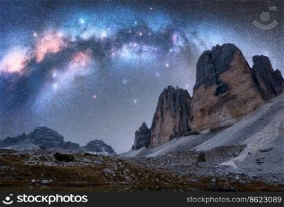 Milky Way arch over mountain peaks at night in summer. Beautiful landscape with blue sky with arched milky way and bright stars, high rocks. Tre Cime in Dolomites, Italy. Space and galaxy. Travel