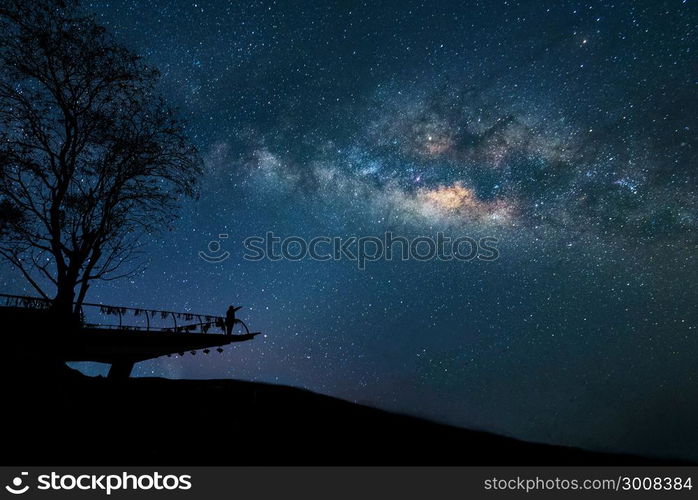 Milky Way at night. Colorful night sky with stars and silhouette of a standing happy man with raised-up arms on the mountain. Freedom travel on long weekend vacation.