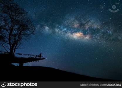Milky Way at night. Colorful night sky with stars and silhouette of a standing happy man with raised-up arms on the mountain. Freedom travel on long weekend vacation.