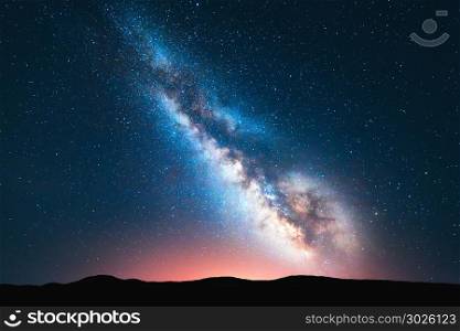 Milky Way. Fantastic night landscape with bright milky way, sky full of stars, yellow light and hills. Shiny stars. Picturesque scene with our universe. Space background. Amazing astrophotography
