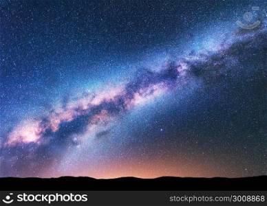 Milky Way. Fantastic night landscape with purple milky way, sky full of stars, yellow light and hills. Shiny stars. Beautiful scene with universe. Space background with starry sky. Astrophotography.