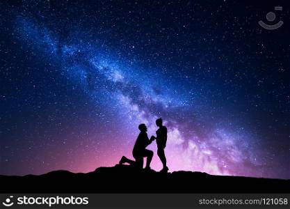 Milky Way. Night landscape with silhouettes of a man making marriage proposal to his girlfriend and starry sky. Silhouette of lovers. Couple, relationship. Milky way with people. Universe