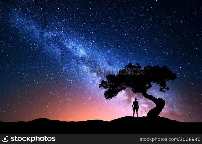 Milky Way. Night sky with stars, old tree and silhouette of a standing alone man on the mountain. Milky way with red light and man on the hill. Galaxy. Silhouette of a man under the tree. Universe