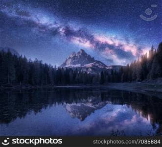 Milky Way over Antorno lake at night. Summer landscape with alpine mountains, trees, purple sky with milky way and stars, beautiful reflection in water, high rocks. Dolomites, Italy. Space and nature