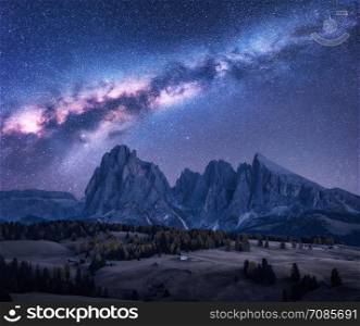 Milky Way over beautiful mauntains at night. Autumn landscape with mountains, purple sky with stars and bright milky way, buildings, trees, high rocks. Alpe di Siusi in Dolomites, Italy. Space