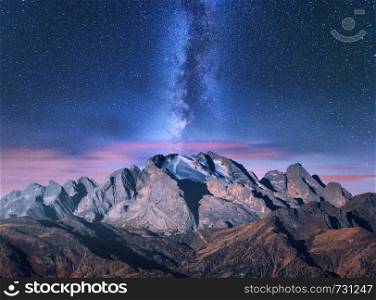 Milky Way over mountains at starry night in autumn. Amazing landscape with alpine mountains, trees, sky with pink clouds, milky way and stars, high rocks. Dolomites, Italy. Space. Beautiful nature