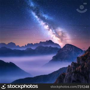 Milky Way over mountains in fog at night in summer. Landscape with alpine mountain valley, purple low clouds, colorful starry sky with milky way. Passo Giau, Dolomites, Italy. Space. Beautiful nature