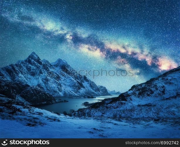 Milky Way over snow covered mountains and sea coast at night in winter in Norway. Landscape with snowy rocks, blue starry sky, colorful galaxy, beautiful fjord. Lofoten Islands, Norway. Space