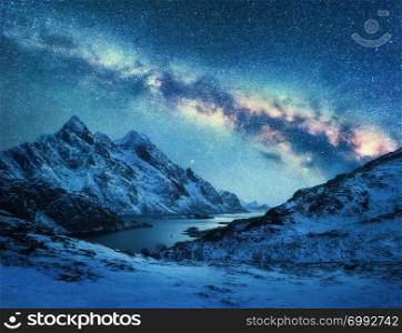 Milky Way over snow covered mountains and sea coast at night in winter in Norway. Landscape with snowy rocks, blue starry sky, colorful galaxy, beautiful fjord. Lofoten Islands, Norway. Space