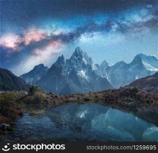 Milky Way over snowy mountains and lake at night. Landscape with snow covered high rocks and starry sky reflected in water in Nepal. Sky with stars. Fantastic view with bright milky way in Himalayas
