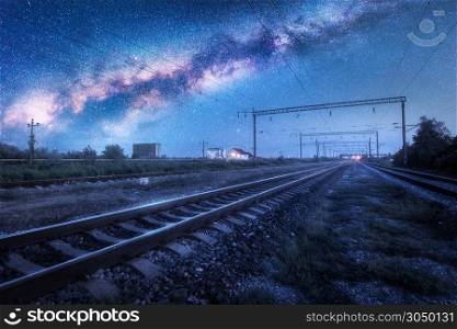 Milky Way over the railway station at starry night. Beautiful industrial landscape with blue sky and stars, galaxy, railroad and buildings at dusk. Railway platform and space in summer. Technology