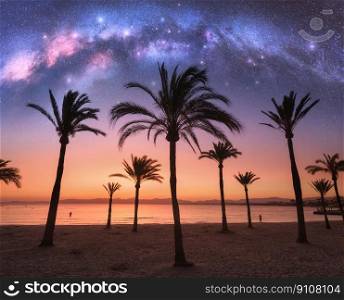 Milky Way over the sandy beach with palms at night in summer. Landscape with sea shore, beautiful starry sky, galaxy and silhouettes of palm trees at sunset. Travel in Mallorca, Spain. Space. Concept