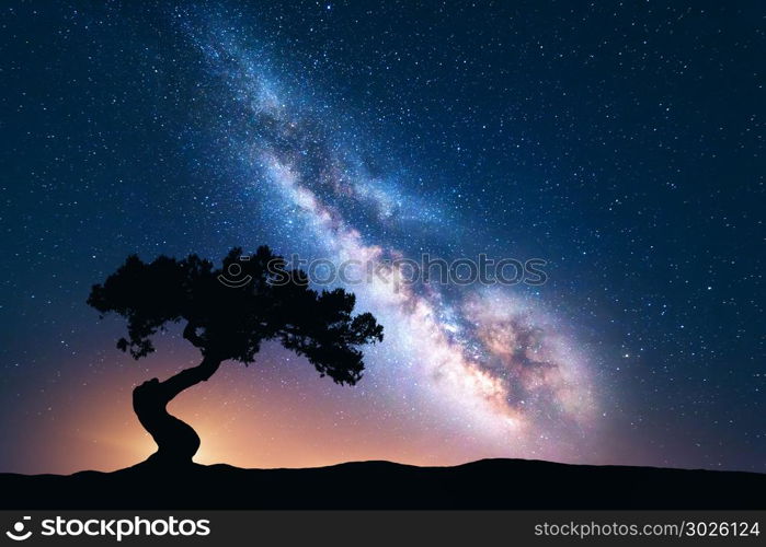 Milky Way with alone old crooked tree on the hill. Colorful night landscape with bright milky way, starry sky and tree in summer. Space background. Amazing astrophotography. Beautiful universe. Travel