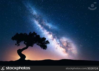 Milky Way with alone old crooked tree on the hill. Colorful night landscape with bright milky way, starry sky and tree in summer. Space background. Amazing astrophotography. Beautiful universe. Travel