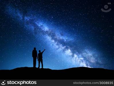 Milky Way with silhouette of a family. Father and a son who pointing finger in night starry sky on the mountain. Night landscape. Silhouette of men on the background of beautiful universe. Space. Blue sky full of stars