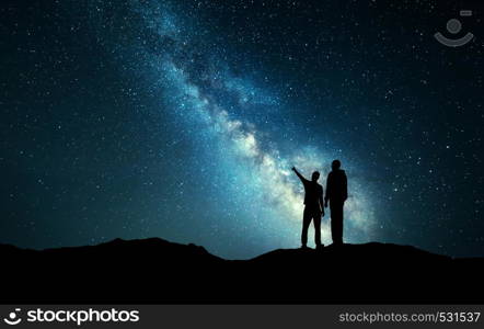 Milky Way with silhouette of a family. Father and a son who pointing finger in night starry sky on the mountain. Night landscape. Beautiful Universe. Space. Travel background with sky full of stars