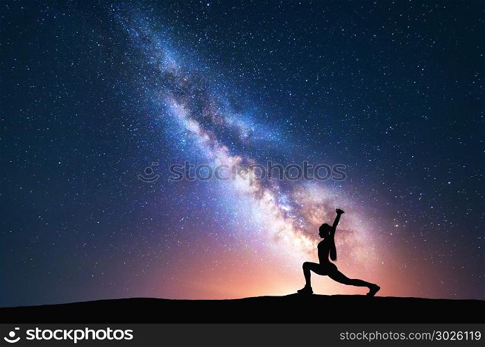 Milky Way with silhouette of a standing woman practicing yoga on the field. Beautiful landscape with meditating girl against night starry sky with bright milky way. Amazing galaxy. Universe. Fitness