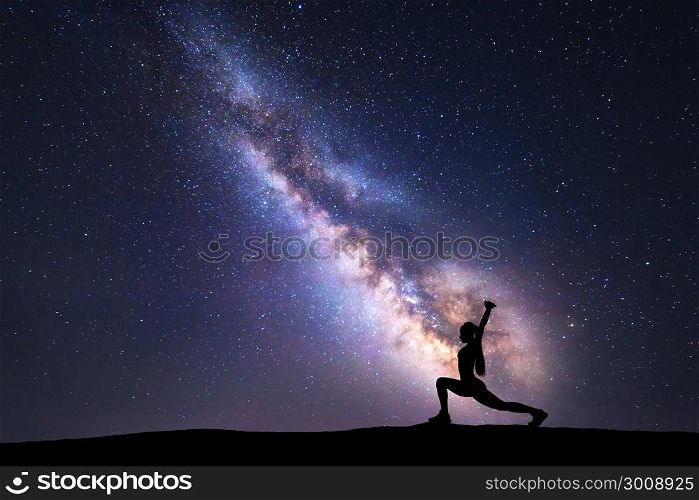 Milky Way with silhouette of a standing woman practicing yoga on the mountain. Beautiful landscape with meditating girl against night starry sky with milky way. Amazing galaxy. Universe. Fitness